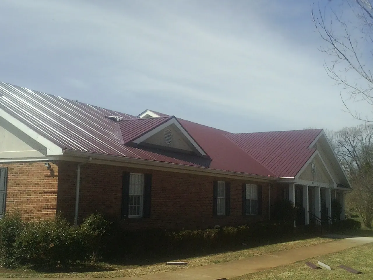 Red metal roof with gabled entries on a long brick building, from a Hail Damage Roof Repair job in Eldon